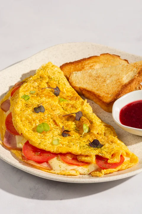 Folded omelette with ham, cheese and tomato, served with toast and berry jam