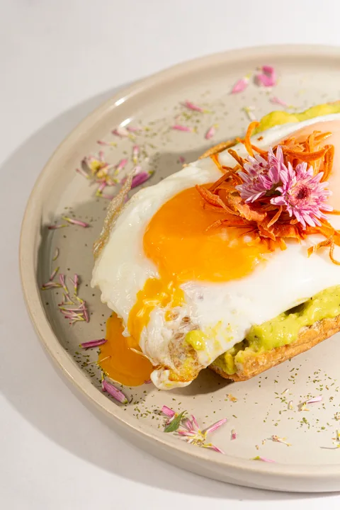 Fried egg on avocado toast, finished with a pink edible flower
